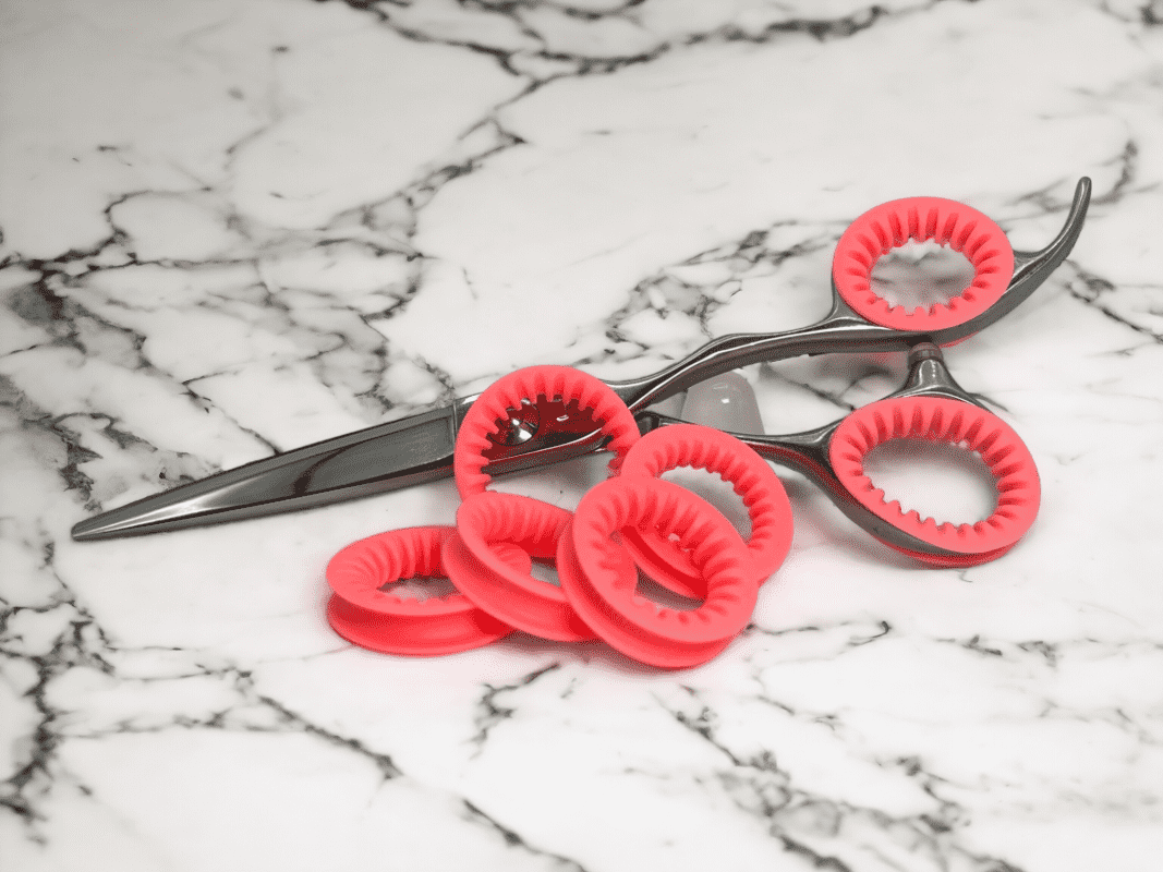 Set of Coral Pink ShearRings with a set inside a pair of haircutting shears, on a marble background